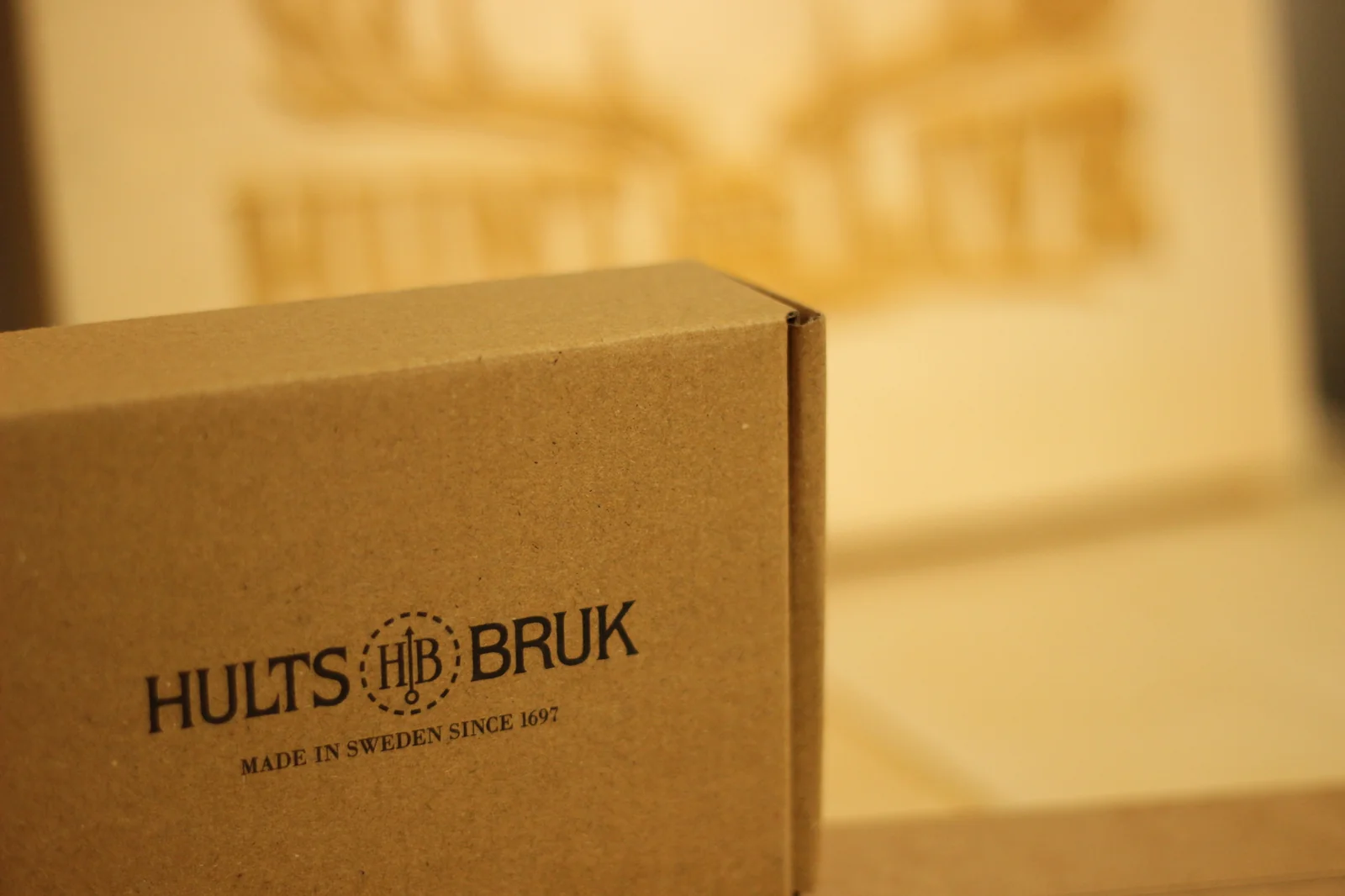 Close-up corner of the Hults Bruk grinding stone box showing the wood-grain background of the kraft cardboard