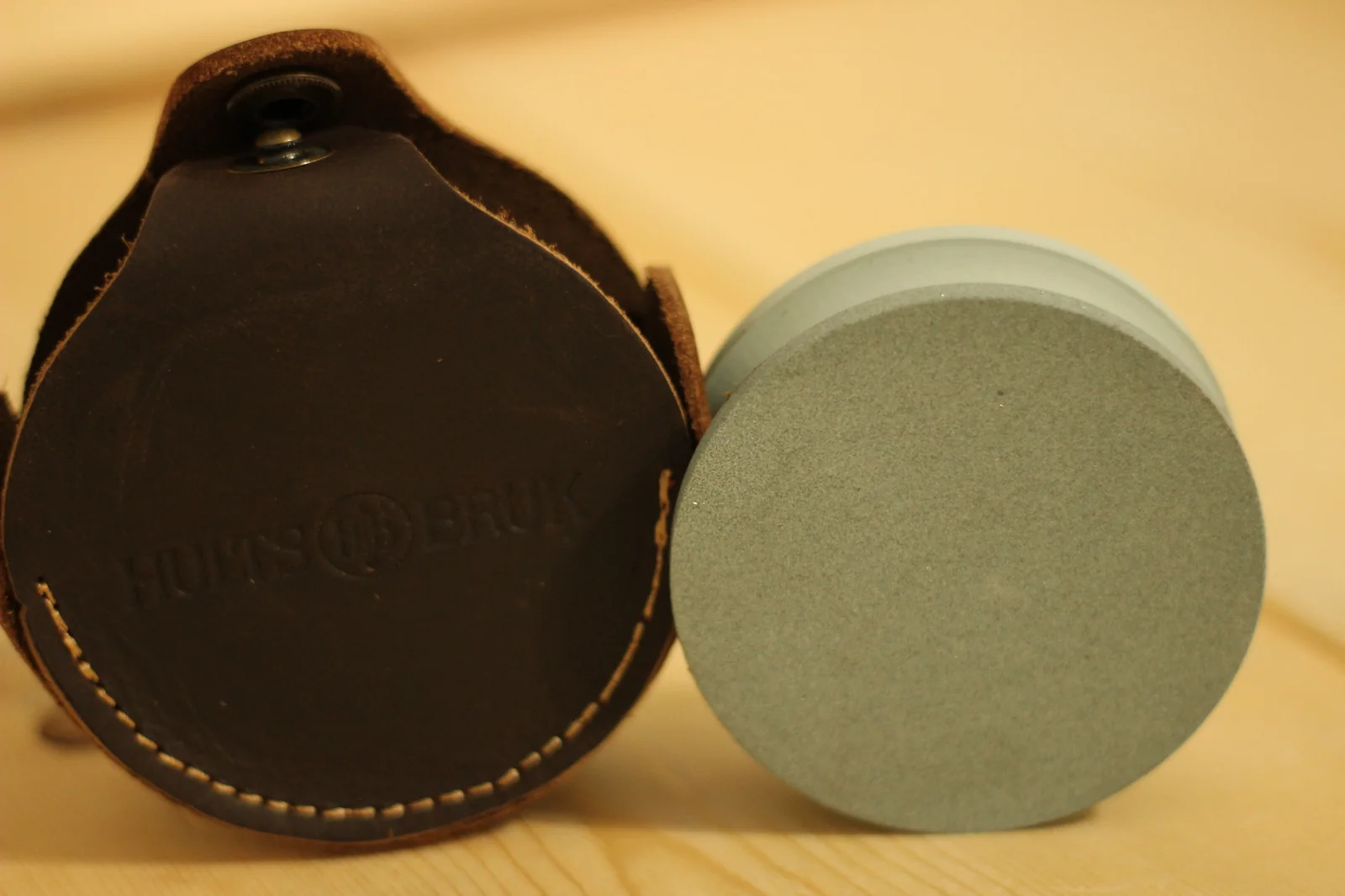 Grinding stone shown out of its leather pouch standing on edge beside the open pouch with HULTS BRUK embossing visible