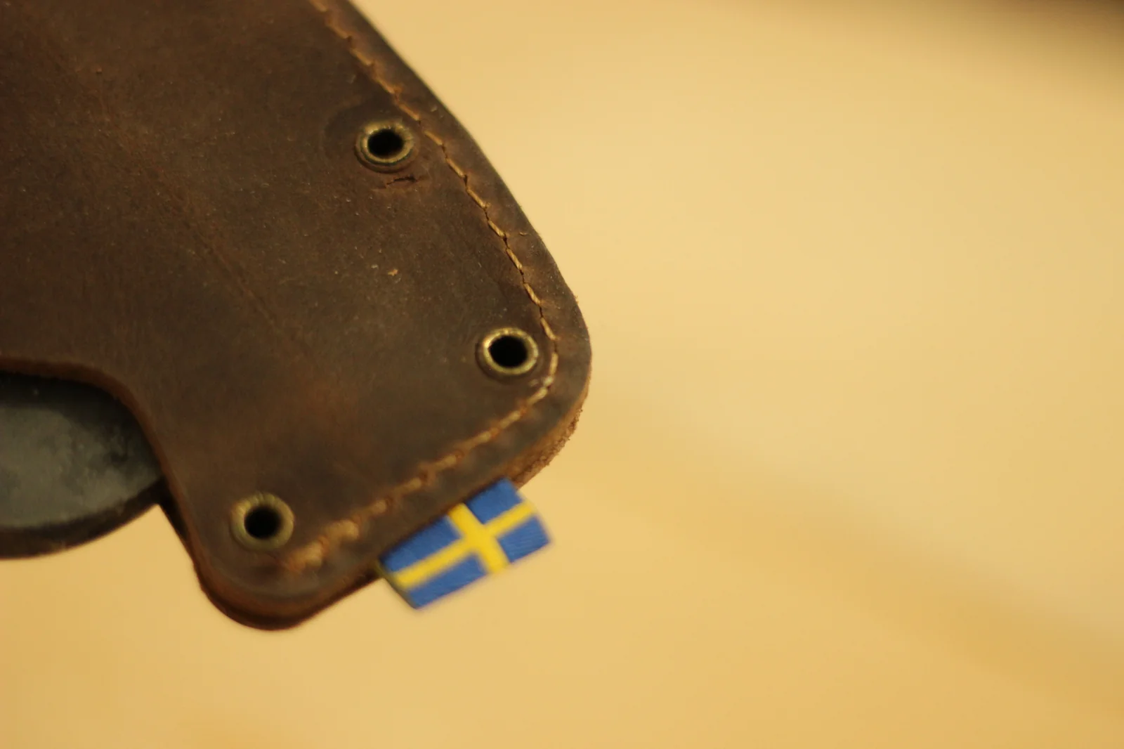 Sheath edge with brass rivets, hand stitching, and a small Swedish flag tag tucked into the seam