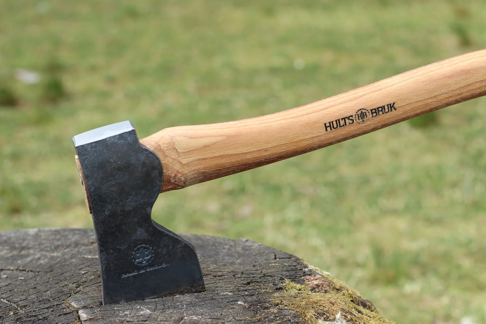 Close-up of the Hults Bruk Dvärdala head buried in a tree stump with the HULTS BRUK branded handle extending up to the right