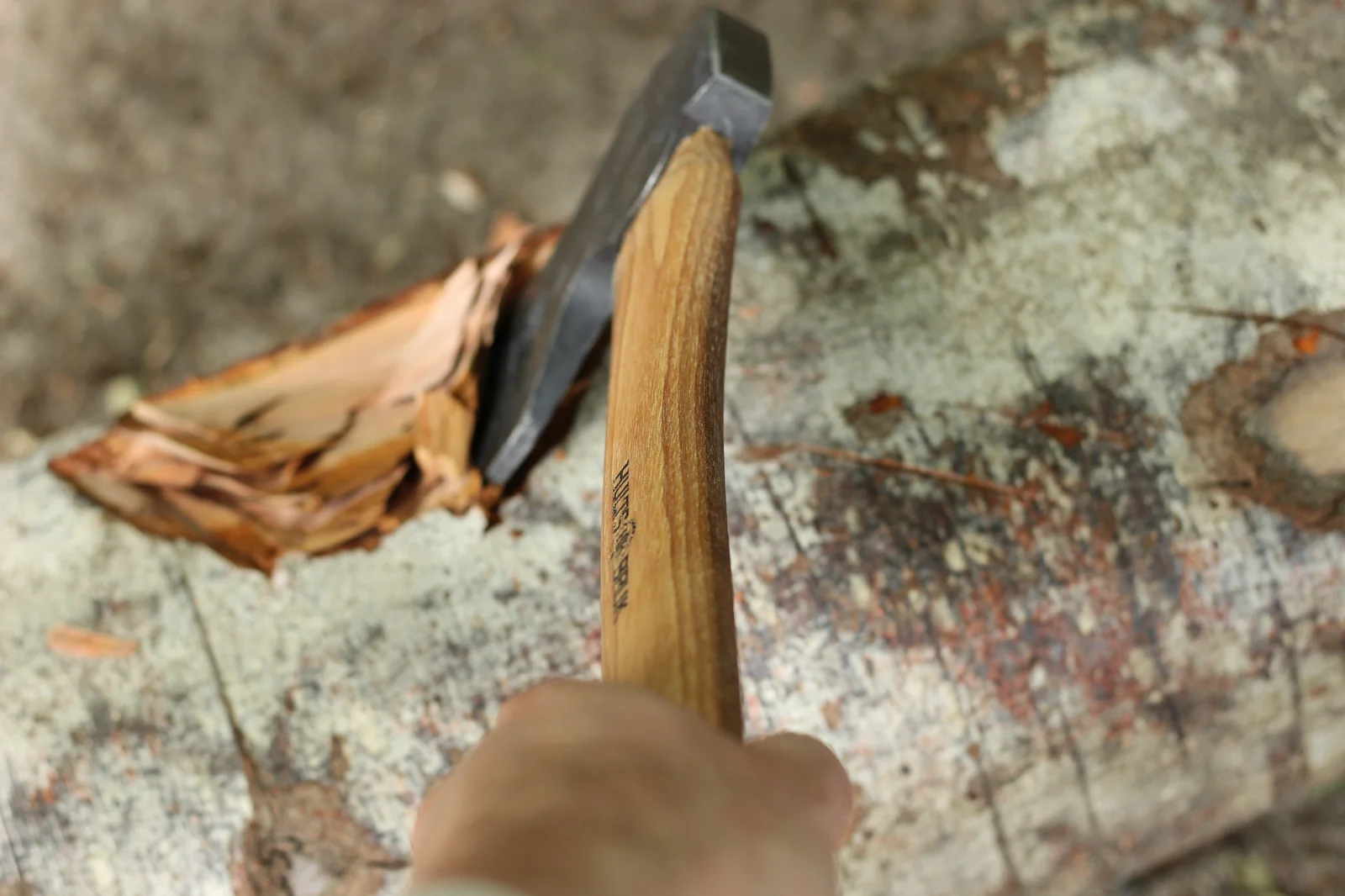 View from behind the axe along the handle looking down at split kindling on a stump with the axe head buried in the wood