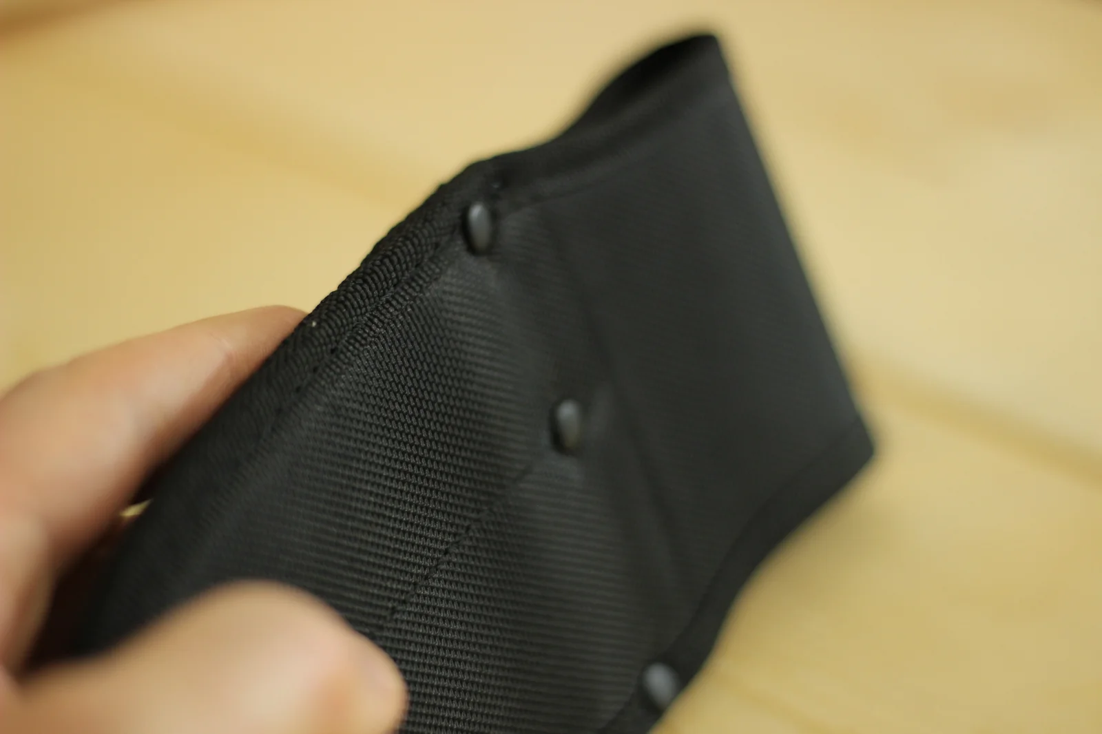 Detail of the sheath edge showing the doubled-stitch binding around the perimeter, reinforcement rivet, and the centerline divider seam between the two blade pockets