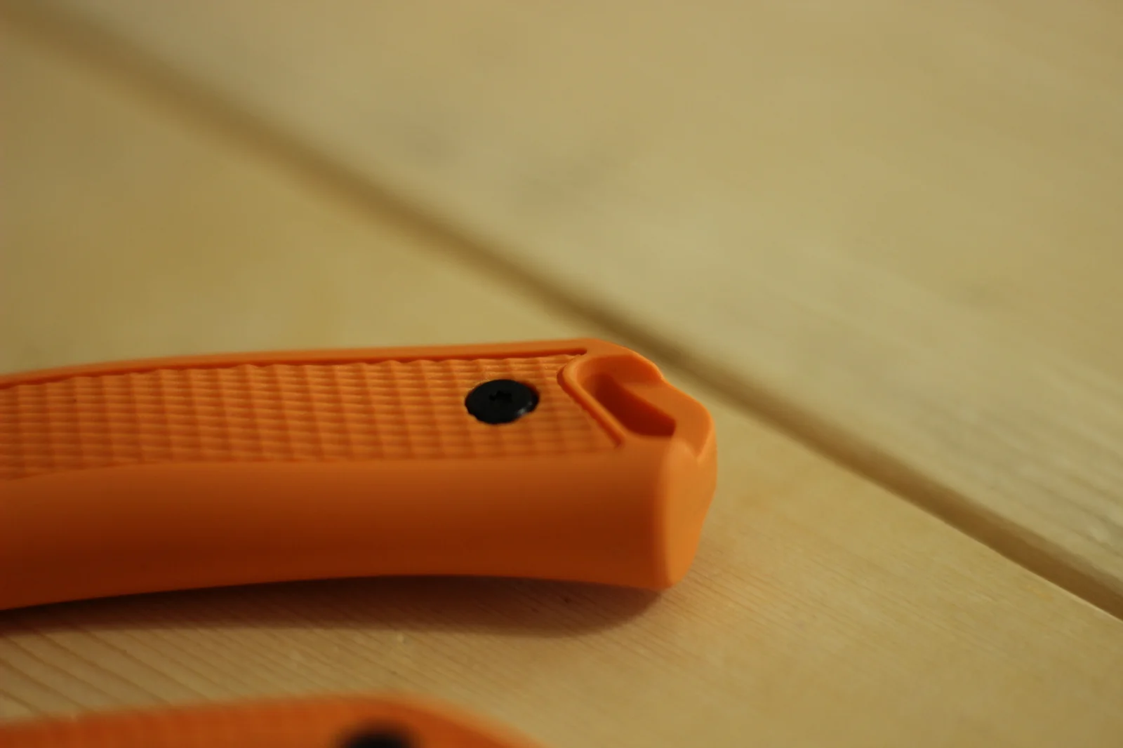 Macro of the textured rubber overlay on the blaze-orange polypropylene handle showing the diamond grip pattern and the recessed thumb-side groove