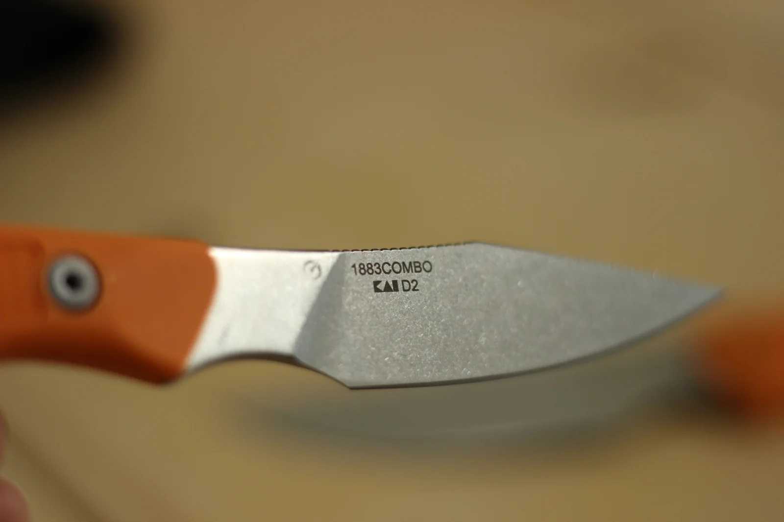 The 1882 blade in macro showing the 1883COMBO and KAI D2 laser-etched markings on the stonewashed blade with the orange handle visible