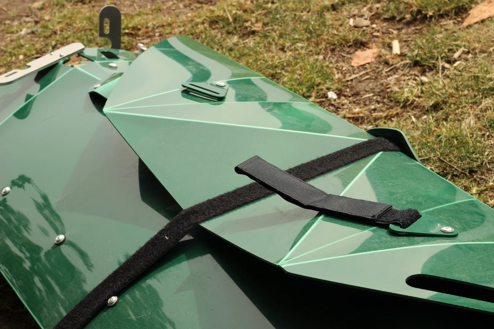 Folded green Tucktec Pro kayak hull on the ground with black retaining strap