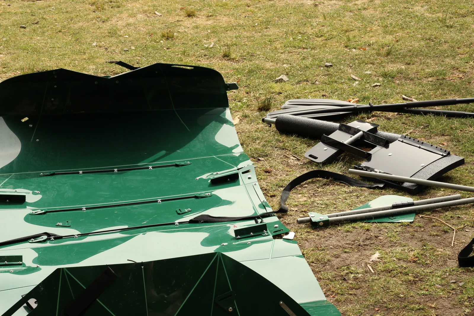 Partially unfolded Tucktec green hull laid out flat on grass next to the separately-purchased paddle, foam stabilizer, and seat-back hardware
