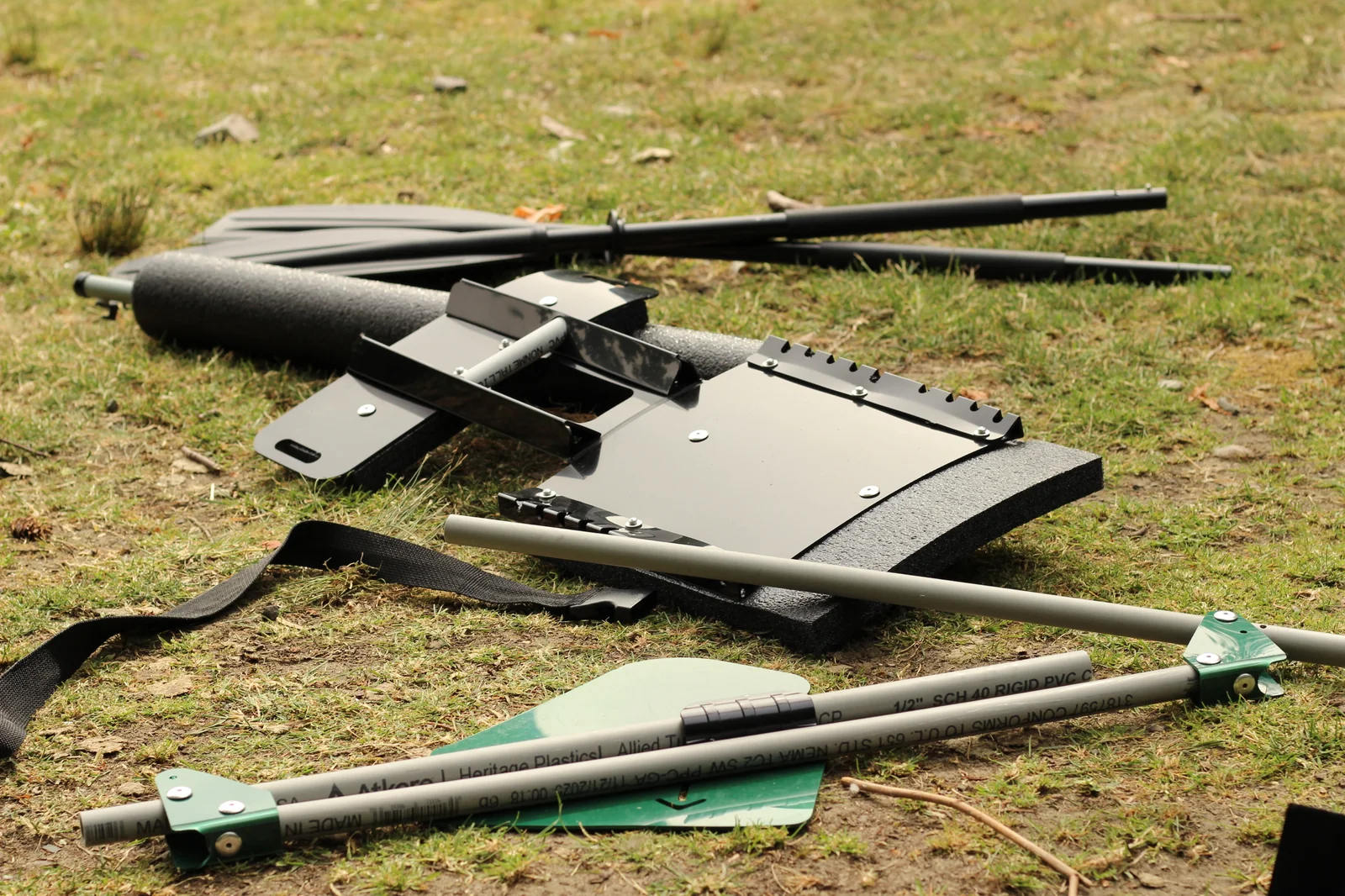 The complete loose kit on grass — the separately-purchased 2-part paddle shaft and blade, included foam stabilizer pontoon, and the included black seat-back hardware piece with mounting frame