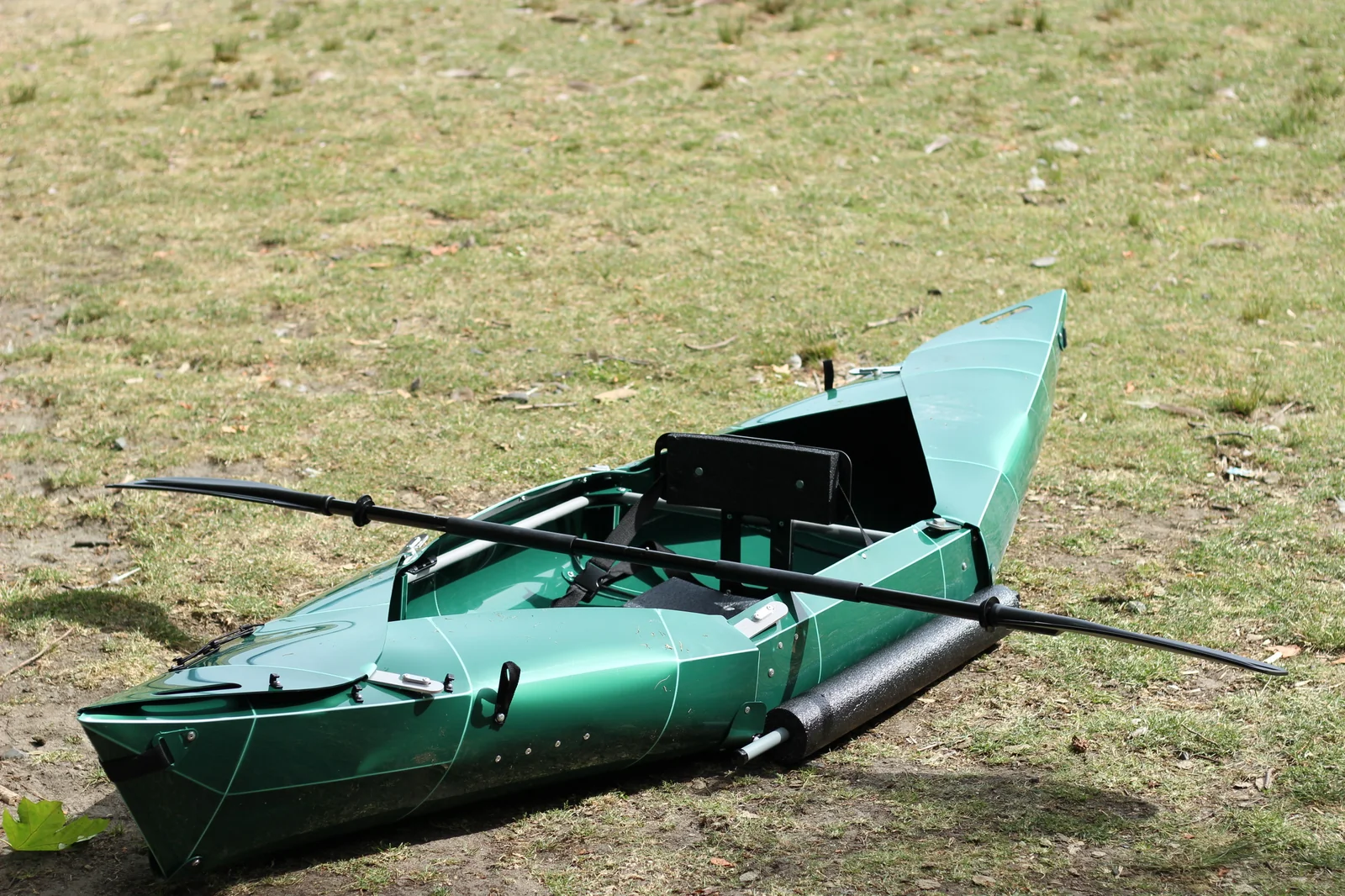 Tucktec Pro folding kayak fully assembled on grass, side view, with the 2-part paddle resting across the cockpit and the foam stabilizer attached