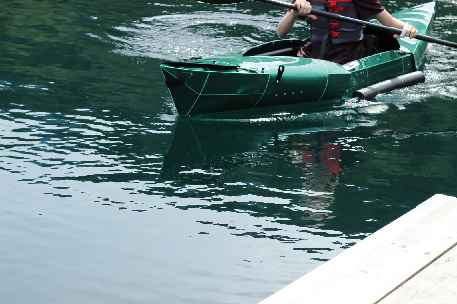 Tucktec Pro kayak from a low water angle with the paddler mid-frame and the bow profile reflected on the calm water surface