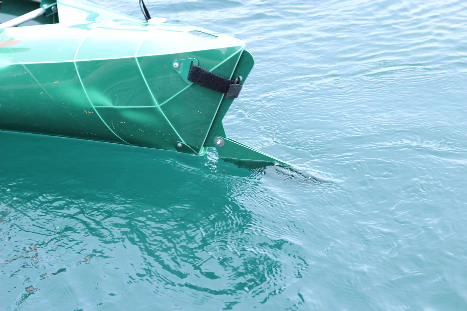 Close-up of the bow of the Tucktec Pro kayak in the water showing the velcro retaining strap and a small skeg fin visible below the waterline
